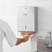 A man putting a paper towel in a Lavex stainless steel paper towel dispenser on a wall.