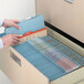 A person's hands holding a blue Smead heavy weight classification folder in a file drawer.