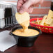 A person dipping a potato chip into a bowl of Fabri-Kal microwaveable side dish bowl filled with cheese sauce.