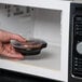 A hand holding a Fabri-Kal plastic container with food in a microwave.