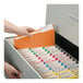 A hand putting an orange Smead file folder into a file drawer with other file folders.