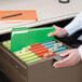 A person putting Smead assorted colored file folders in a file drawer.