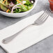 A Chef & Sommelier stainless steel salad fork on a napkin next to a bowl of salad.