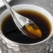 A Chef & Sommelier stainless steel teaspoon in a cup of coffee with sugar.