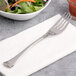 A Chef & Sommelier stainless steel salad fork on a napkin next to a bowl of salad.