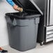 A man putting a coffee cup into a Rubbermaid BRUTE trash can in a school kitchen.