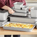 A woman using a Hatco stainless steel half size food pan to prepare food in a school kitchen.