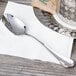 A Chef & Sommelier stainless steel teaspoon on a napkin on a table.