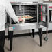 A man in a white shirt putting food in a Vulcan convection oven.