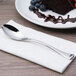 A plate with a slice of cake and a Chef & Sommelier stainless steel dessert spoon on a napkin.