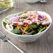 A white porcelain oval bowl filled with salad with mushrooms and onions.