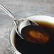 A Chef & Sommelier stainless steel teaspoon in a cup of liquid.