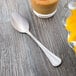 A Libbey stainless steel teaspoon on a table next to a glass of juice.