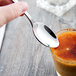 A hand holding a Libbey stainless steel teaspoon over a glass of liquid.