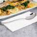 An Arcoroc stainless steel dinner spoon on a white surface in a seafood restaurant near a plate of food.