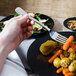 A hand holding a Libbey medium weight dinner fork over a plate of food.