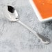 A Libbey stainless steel bouillon spoon next to a bowl of soup.