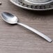 An Arcoroc stainless steel demitasse spoon with a silver handle on a table.
