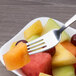 An Arcoroc stainless steel dessert fork holding a piece of fruit.