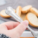 A hand holding a Libbey stainless steel bouillon spoon over a bowl of soup.