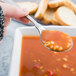 A Libbey stainless steel bouillon spoon full of soup over a bowl.