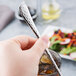 A hand holding a Libbey stainless steel iced tea spoon in front of a glass of ice.