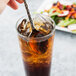 A hand holding a Libbey Aspire stainless steel iced tea spoon in a glass of iced tea with a straw.