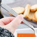 A person holding a Libbey stainless steel bouillon spoon over a bowl of soup.