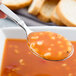 A Libbey stainless steel bouillon spoon full of soup in a bowl.