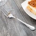 A Libbey stainless steel dessert fork next to a piece of cake on a table.