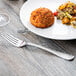 A Libbey stainless steel dinner fork on a table with a plate of food.