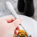 A hand holding a Libbey stainless steel dinner fork over a plate of food.