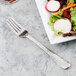 A Libbey stainless steel salad fork next to a plate of salad.