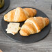 An Epicurean round pizza board with croissants and cheese on a table.