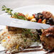 A Chef & Sommelier stainless steel dinner knife cutting a meatball on a plate of food.