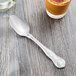 A Libbey stainless steel serving spoon on a table next to a glass of liquid.