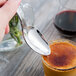 A hand holding a Libbey stainless steel serving spoon over a glass of liquid.