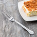 A Libbey stainless steel utility fork on a plate with a piece of cake.