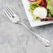 A Libbey stainless steel salad fork next to a plate of salad.