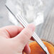 A hand holding a Libbey stainless steel dessert spoon over a bowl of food.