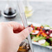 A hand holding a Libbey stainless steel iced tea spoon over a glass of liquid.