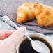 A hand holding a Libbey stainless steel demitasse spoon over a cup of coffee.