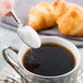 A hand using a Libbey stainless steel demitasse spoon to pour sugar into a cup of coffee.