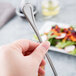 A hand holding a Libbey stainless steel iced tea spoon.