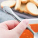 A hand holding a Libbey stainless steel bouillon spoon over a bowl of soup.