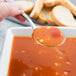 A person holding a Libbey stainless steel bouillon spoon full of soup over a bowl.