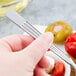 A person holding a Libbey stainless steel cocktail fork over a white object.