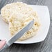 A Libbey stainless steel bread and butter knife spreading butter on a plate of biscuits.