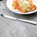 A Libbey stainless steel dinner knife next to a plate of food on a table.