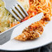 A Libbey stainless steel dinner knife on a plate of food with a fork.